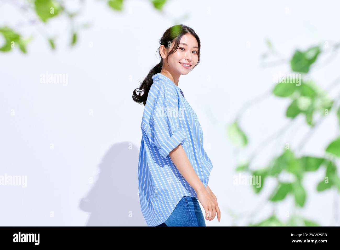 Una donna in camicia a righe blu e bianca davanti a foglie verdi Foto Stock
