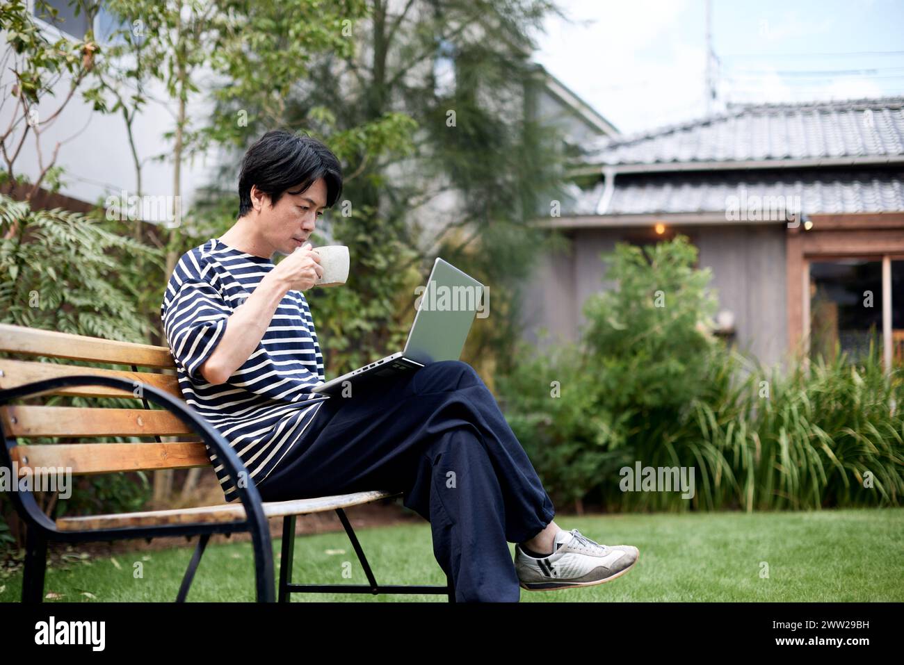 Un uomo seduto su una panchina con un portatile Foto Stock