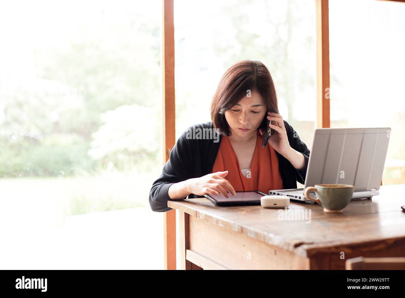 Una donna seduta a un tavolo con un portatile e un telefono Foto Stock