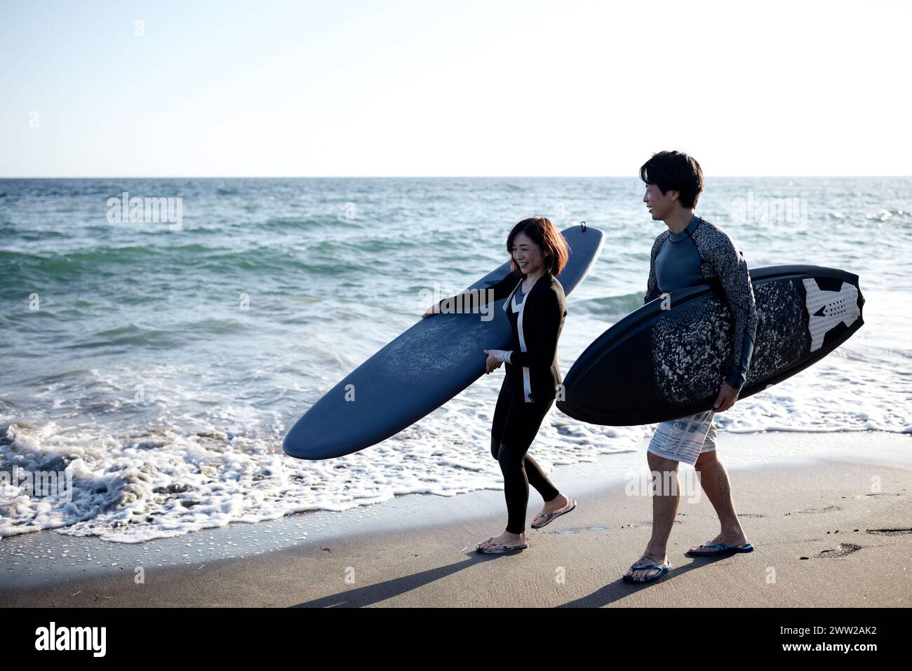 Un uomo e una donna che camminano sulla spiaggia tenendo le tavole da surf Foto Stock