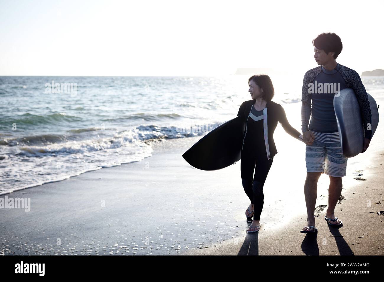 Un uomo e una donna che camminano sulla spiaggia tenendo le tavole da surf Foto Stock
