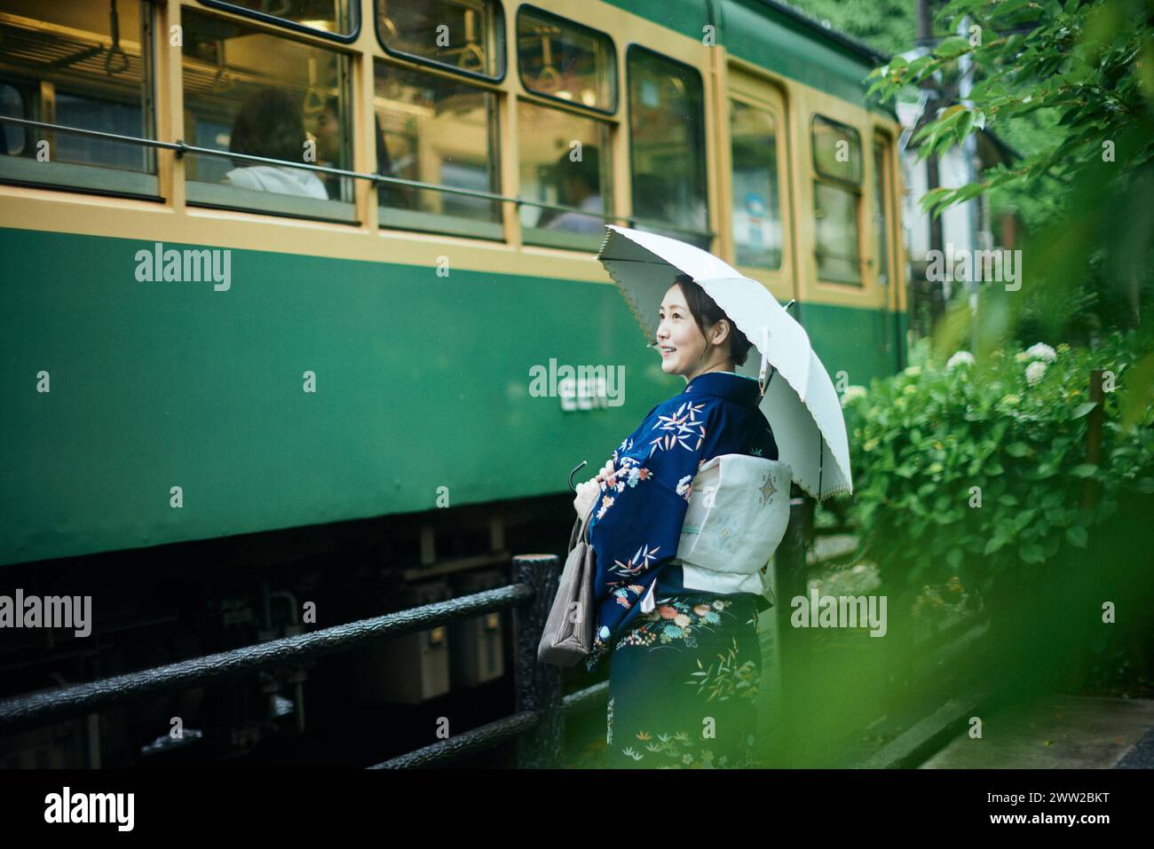 Una donna in kimono si trova accanto a un treno verde Foto Stock