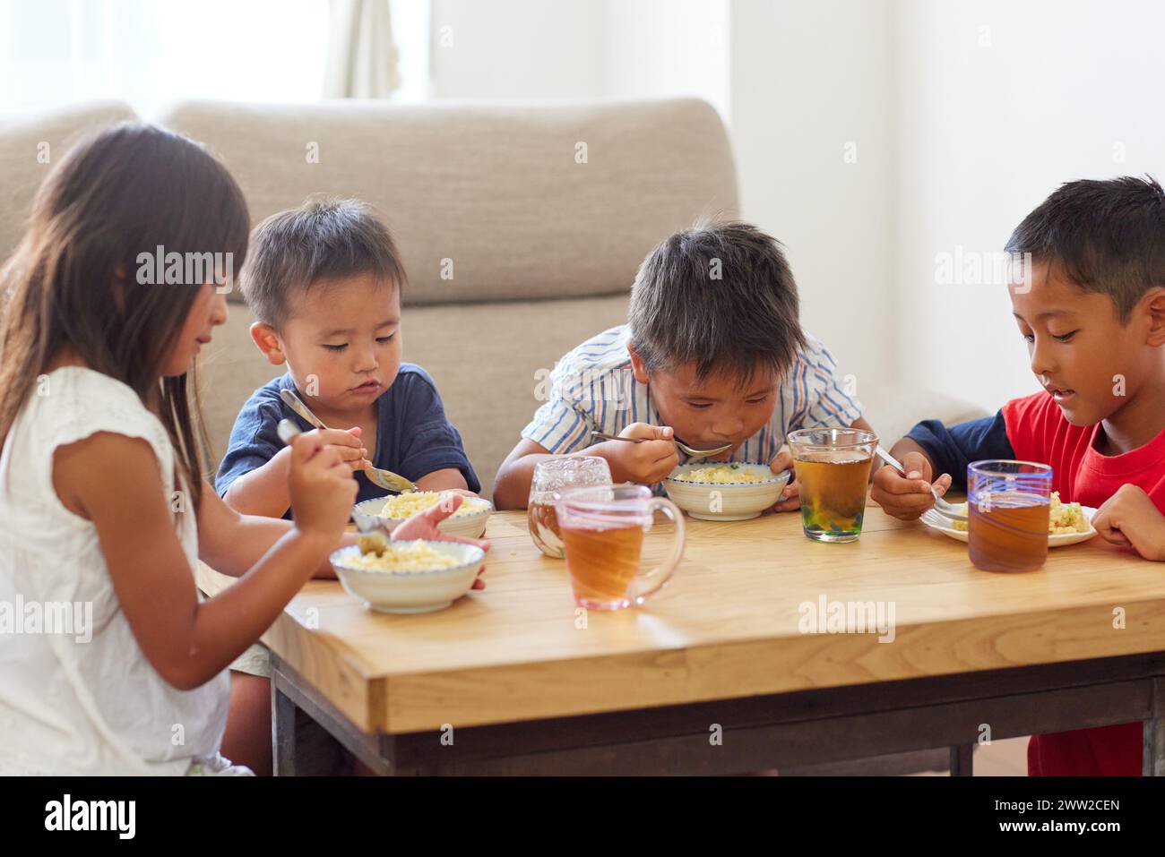 Quattro bambini seduti a un tavolo a mangiare cibo Foto Stock