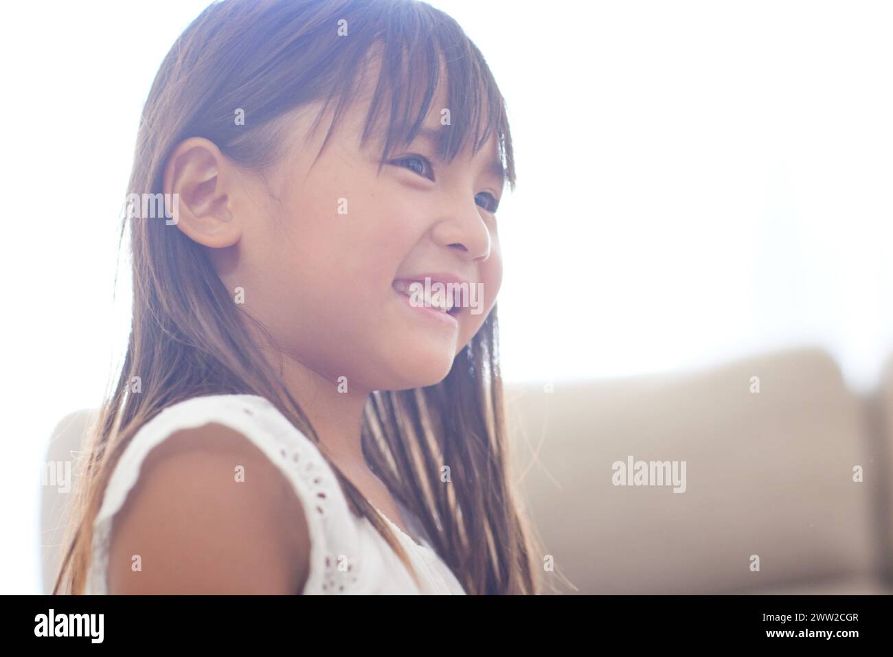 Una bambina sorride mentre si siede su un divano Foto Stock