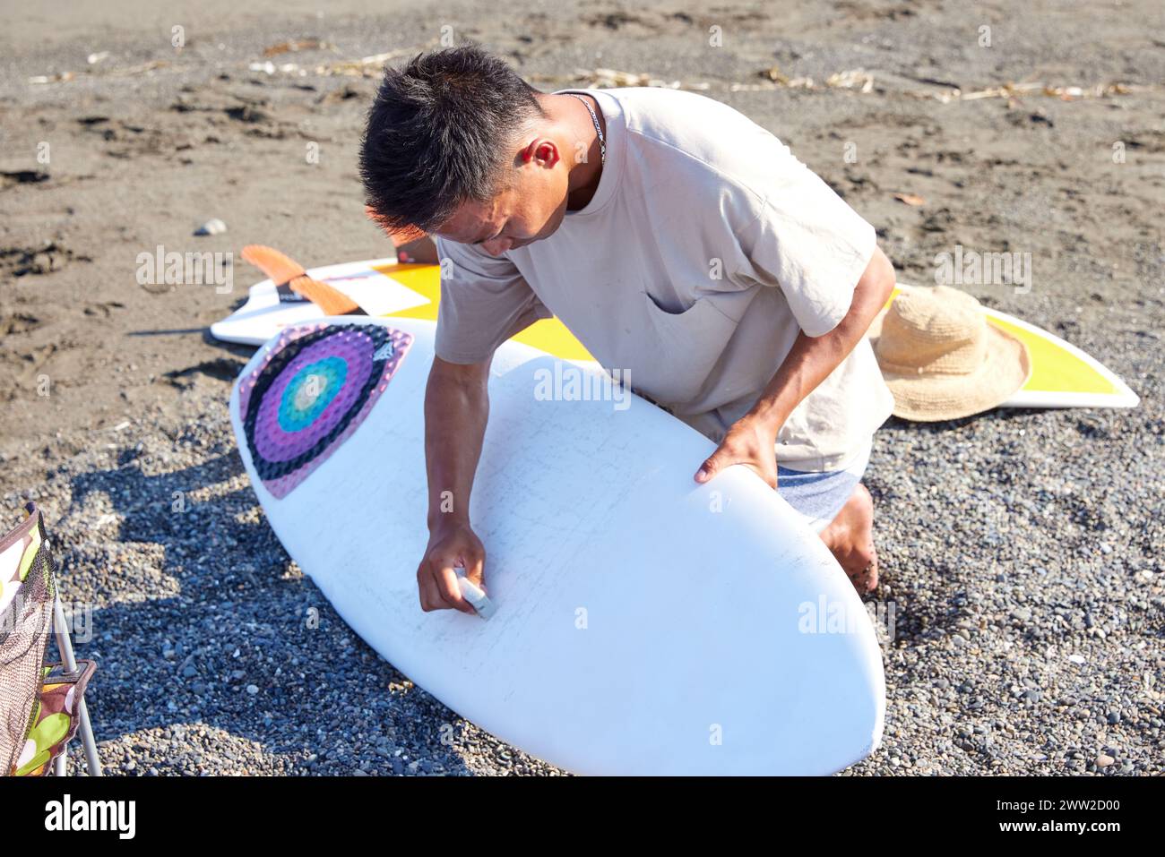 Un uomo seduto sulla spiaggia con una tavola da surf Foto Stock