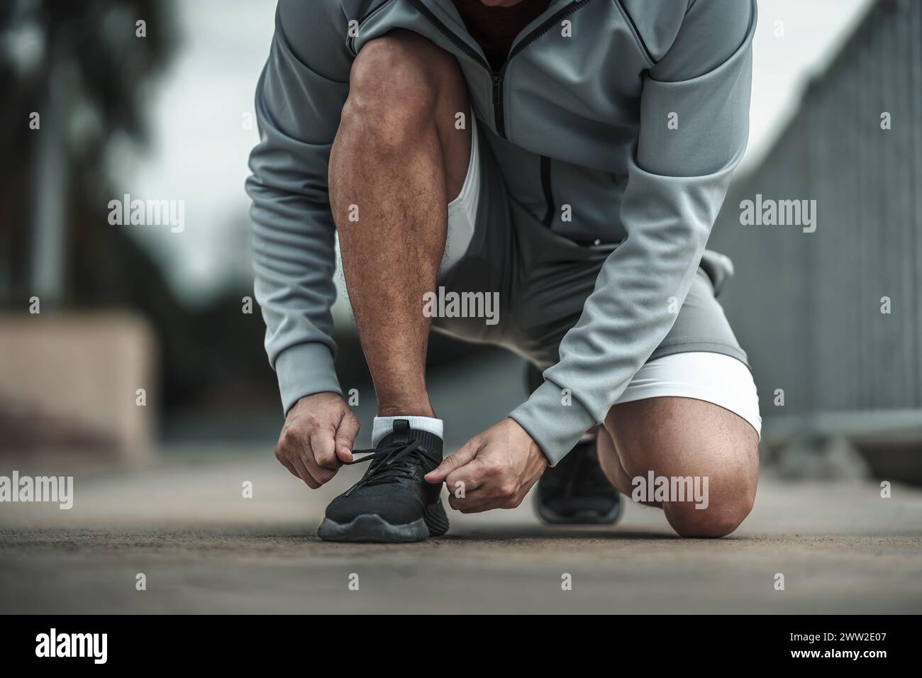 Un uomo che lega scarpe sportive nel parco del centro città prima di allenarsi con il cardio, correre. Concetto di salute e stile di vita nelle grandi città. Foto Stock