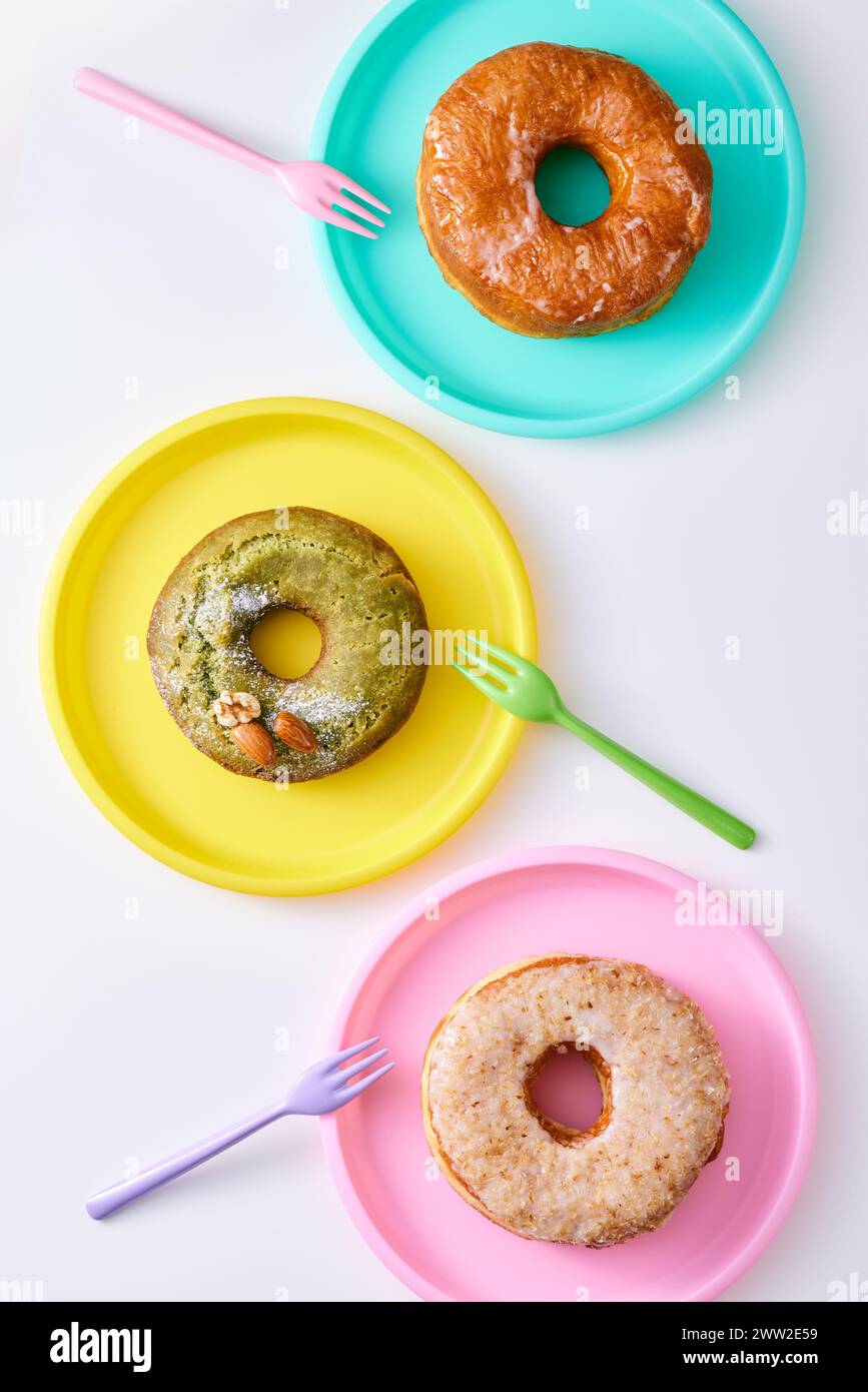 Tre ciambelle su piatti colorati con forchette Foto Stock
