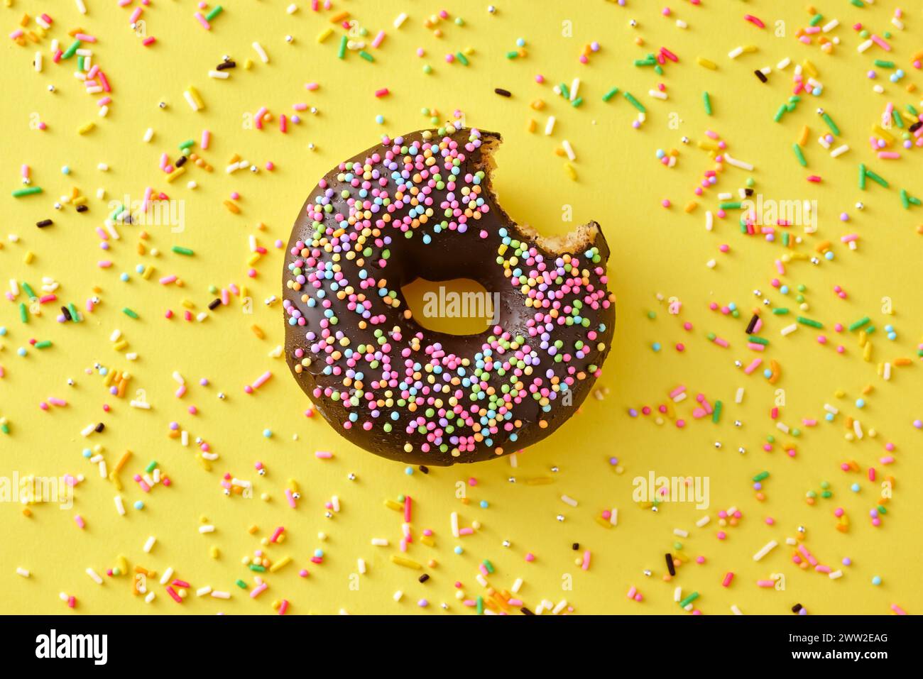 Una ciambella al cioccolato con spruzzi su sfondo giallo Foto Stock