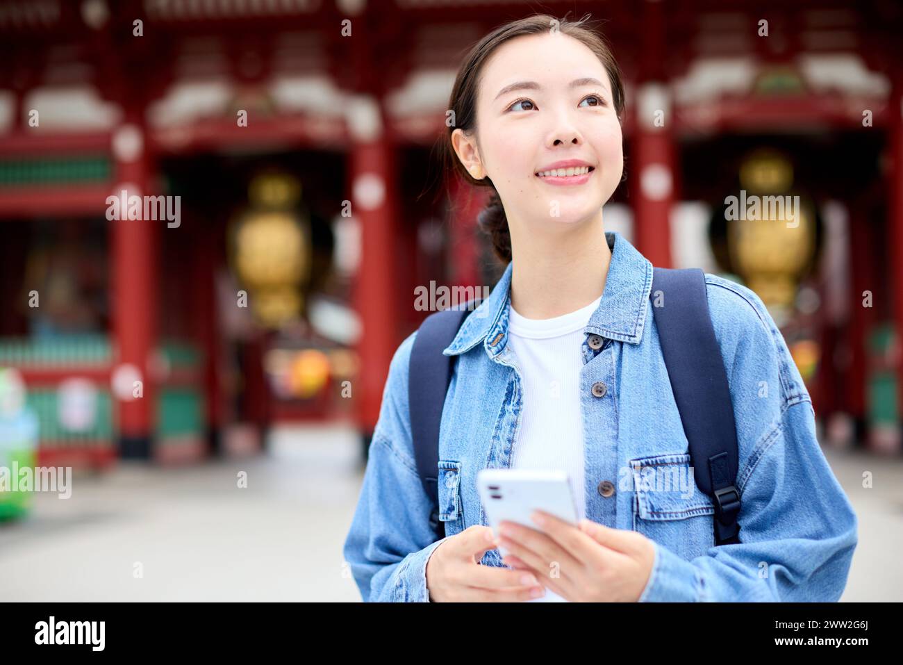 Donna asiatica in giacca di denim e camicia bianca che tiene il cellulare Foto Stock