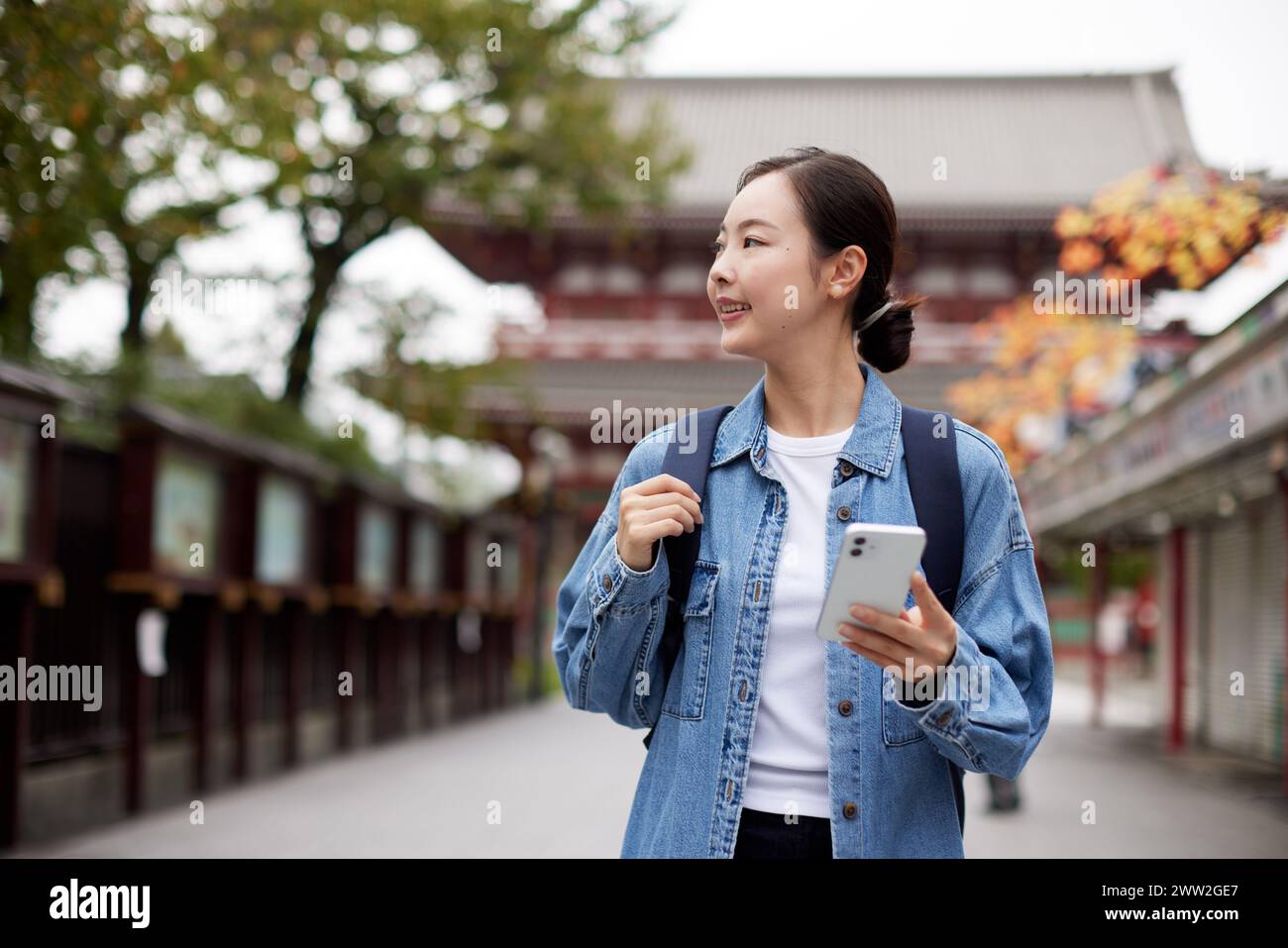 Donna asiatica che cammina per strada tenendo un cellulare Foto Stock