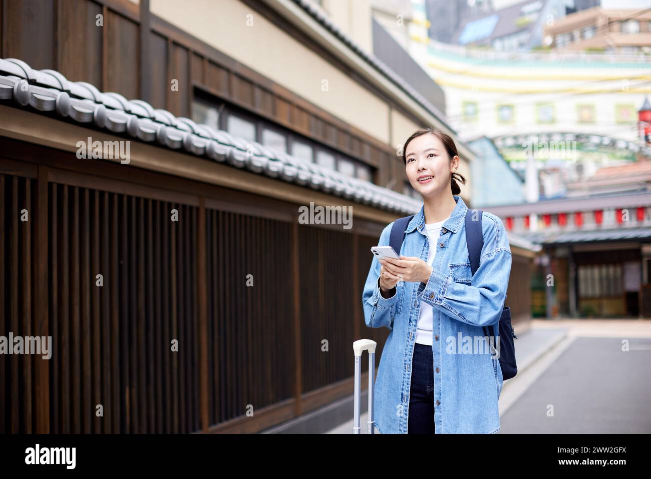 Donna asiatica con valigia e telefono in strada Foto Stock