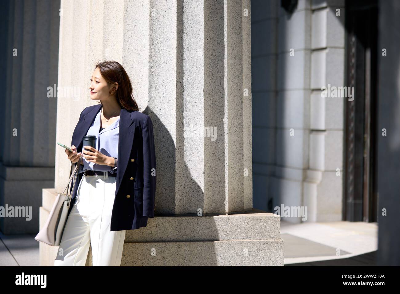 Una donna con un completo e pantaloni bianchi appoggiati a una colonna Foto Stock