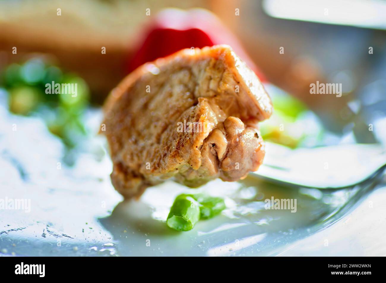 Pezzo di bistecca spiedato sulla forchetta, pepe rosso, germogli di cipolla verde sul piatto, primo piano. Foto Stock