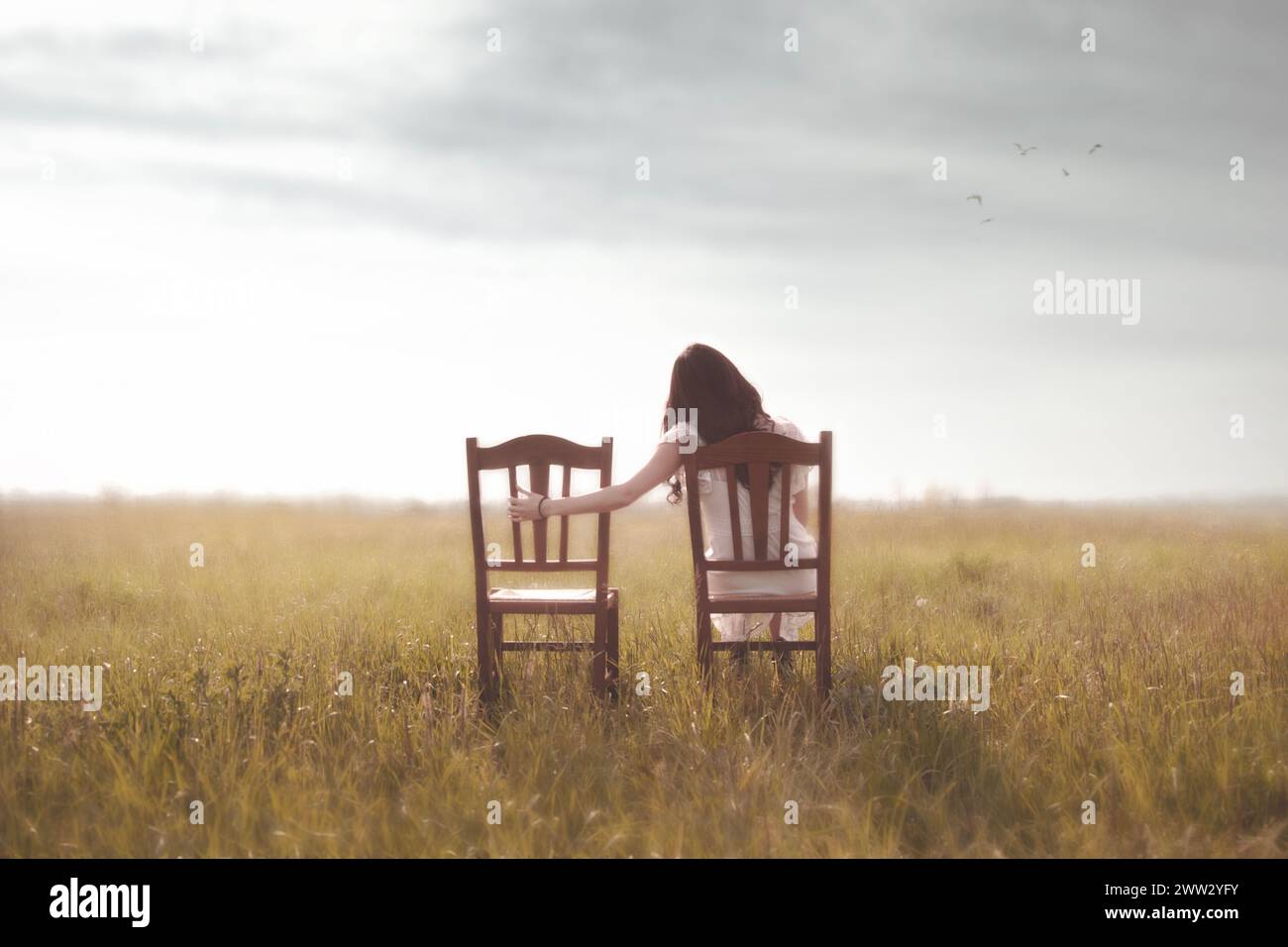 una donna triste guarda nostalgicamente la sedia vuota del suo amante in mezzo alla natura Foto Stock