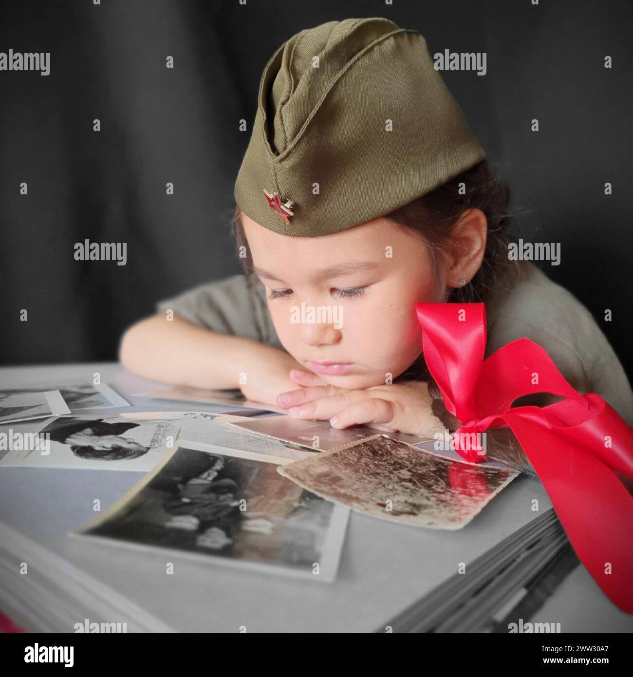 Una bambina in uniforme militare con due trecce e archi rossi sta guardando un album con fotografie. Foto ritratto per il giorno della Vittoria. 9 maggio Foto Stock