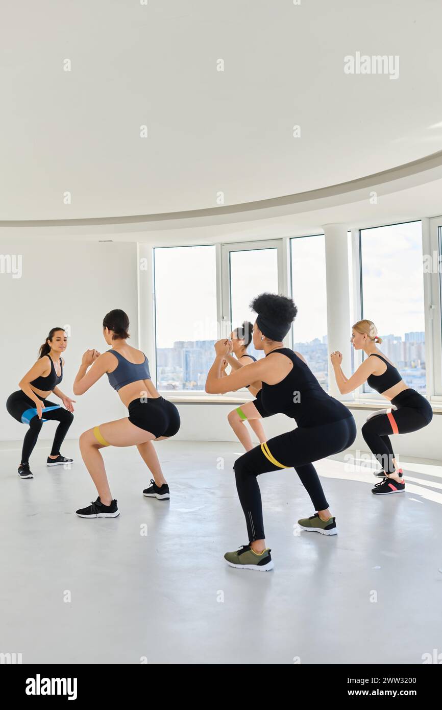 gruppo di diverse donne in abbigliamento sportivo che guardano l'allenatore e squattano con fasce di resistenza Foto Stock