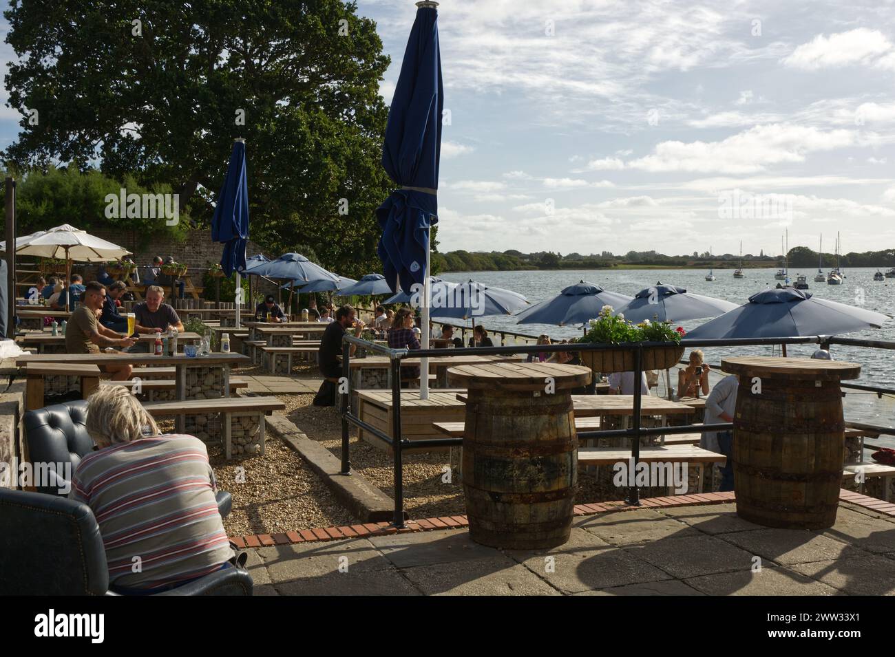Persone che gusteranno cibo e bevande sulla terrazza sul lungomare del pub Crown and Anchor al Dell Quay a Chichester Harbour, West Sussex, Inghilterra Foto Stock