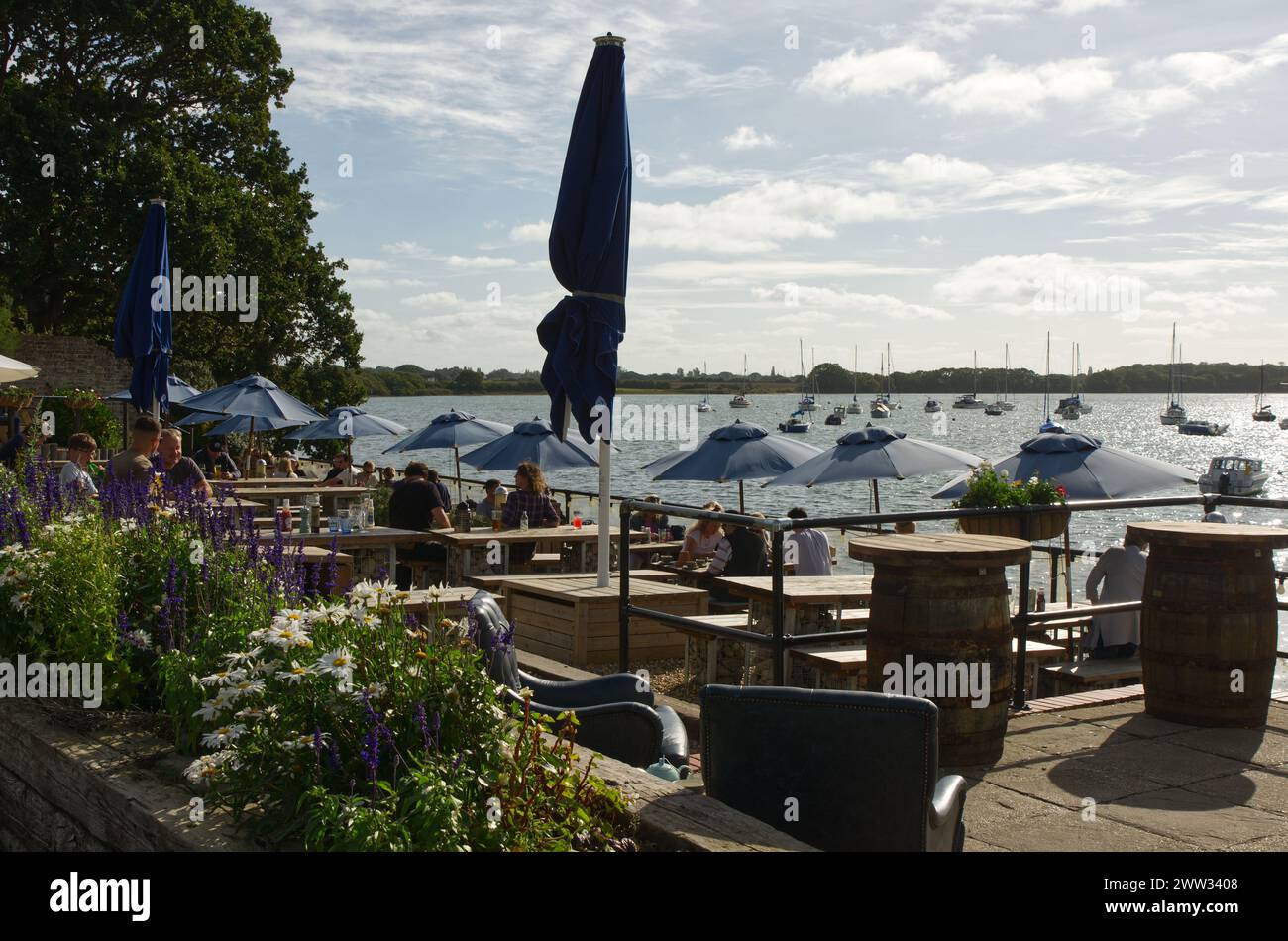 Persone che gusteranno cibo e bevande sulla terrazza sul lungomare del pub Crown and Anchor al Dell Quay a Chichester Harbour, West Sussex, Inghilterra Foto Stock
