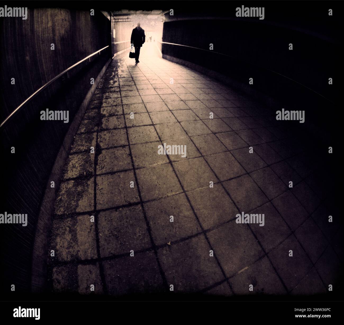 Silhouette dell'uomo che entra in un tunnel scuro in bronzo monocromatico Foto Stock
