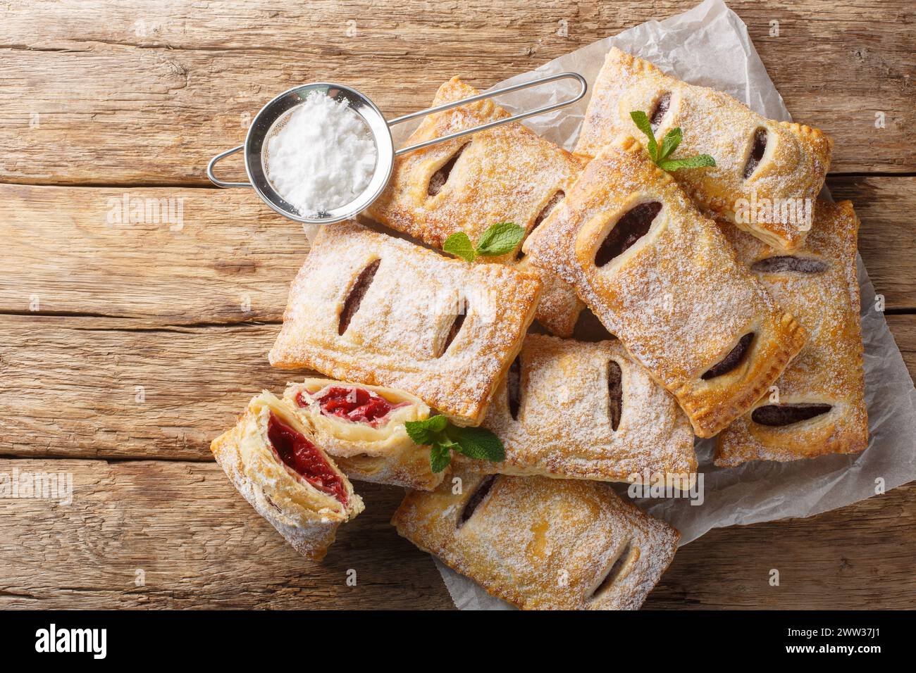 Pasticceria di pasta sfoglia fatta in casa, torte di bacche con zucchero a velo e menta in primo piano sul tavolo. Vista dall'alto orizzontale Foto Stock