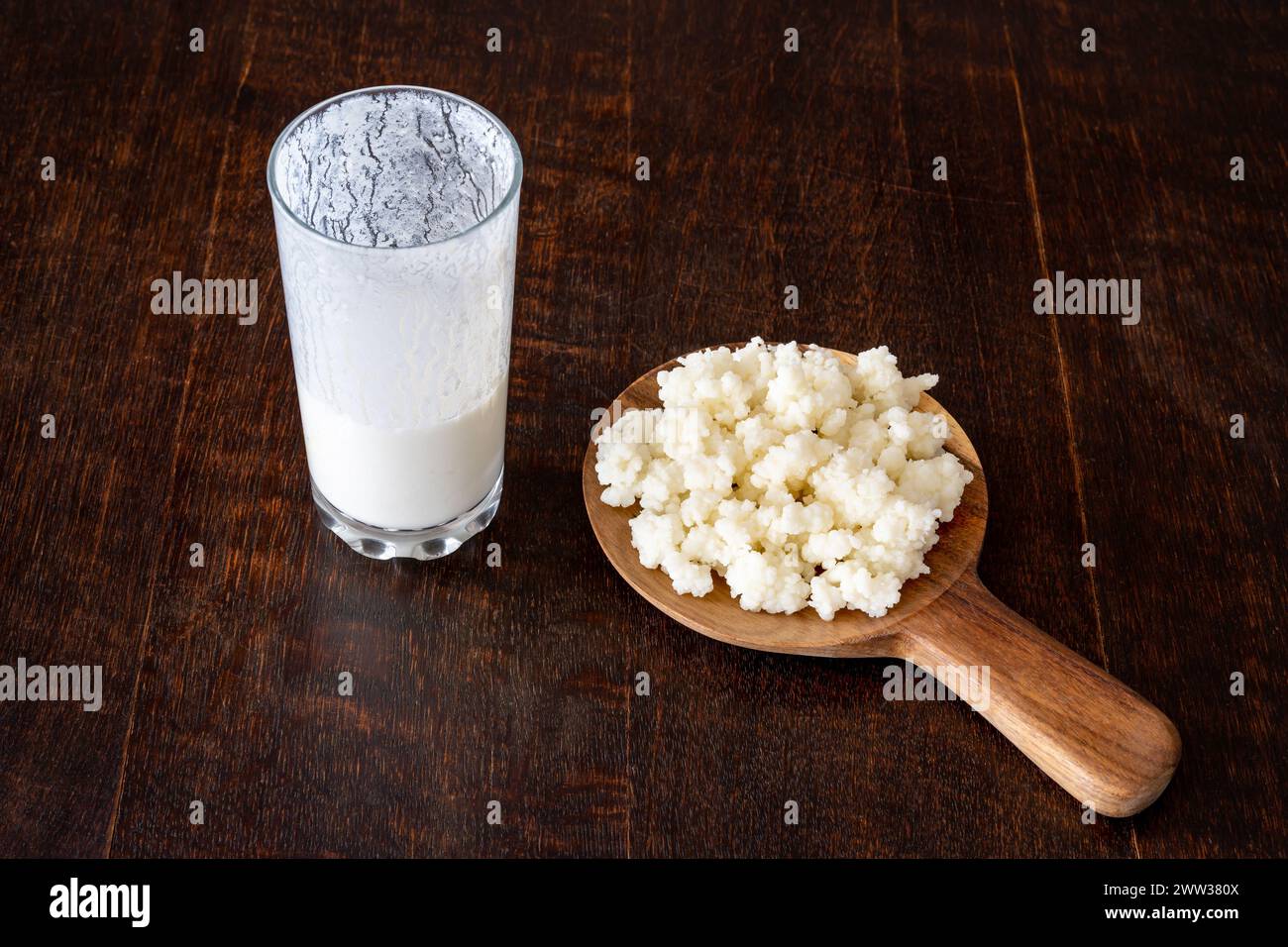 I chicchi di kefir e la bevanda a base di latte fermentato sono isolati su un rustico tavolo di legno Foto Stock