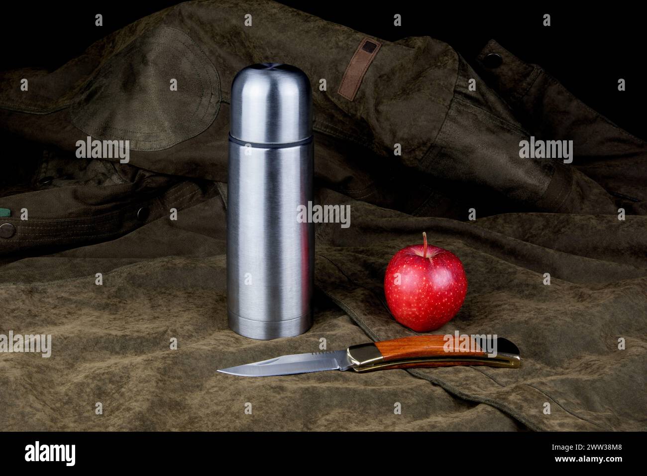 Fiasca sottovuoto con coltello aperto e mela rossa su un camice da campo esterno Foto Stock
