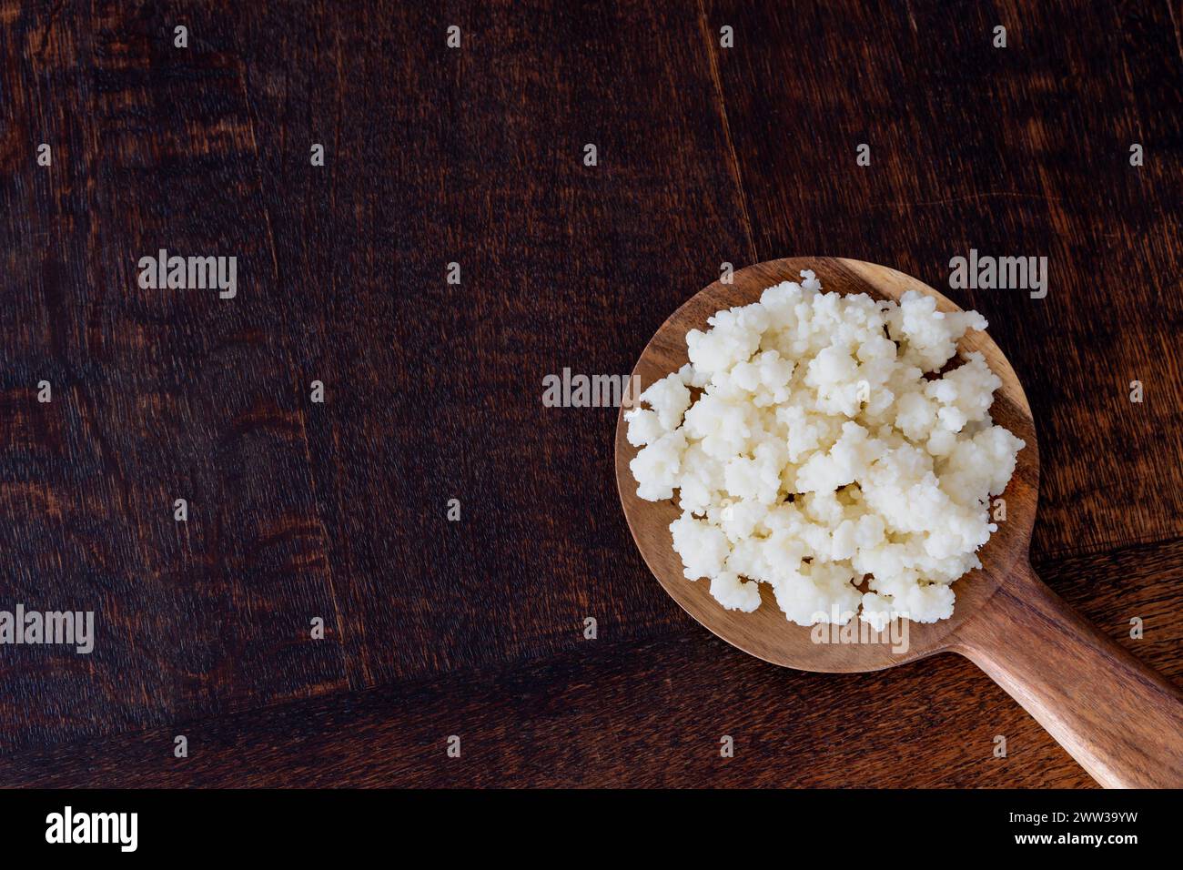 Grani di kefir di latte su cucchiaio di legno isolato, copia spazio Foto Stock
