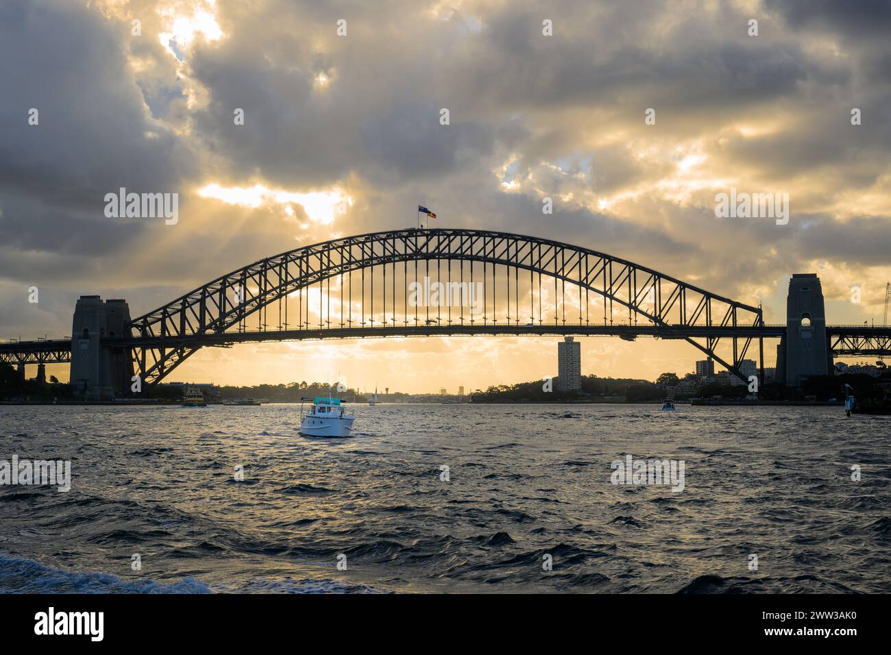 Una piccola barca che naviga sotto il Sydney Harbour Bridge al tramonto, Sydney, Australia Foto Stock