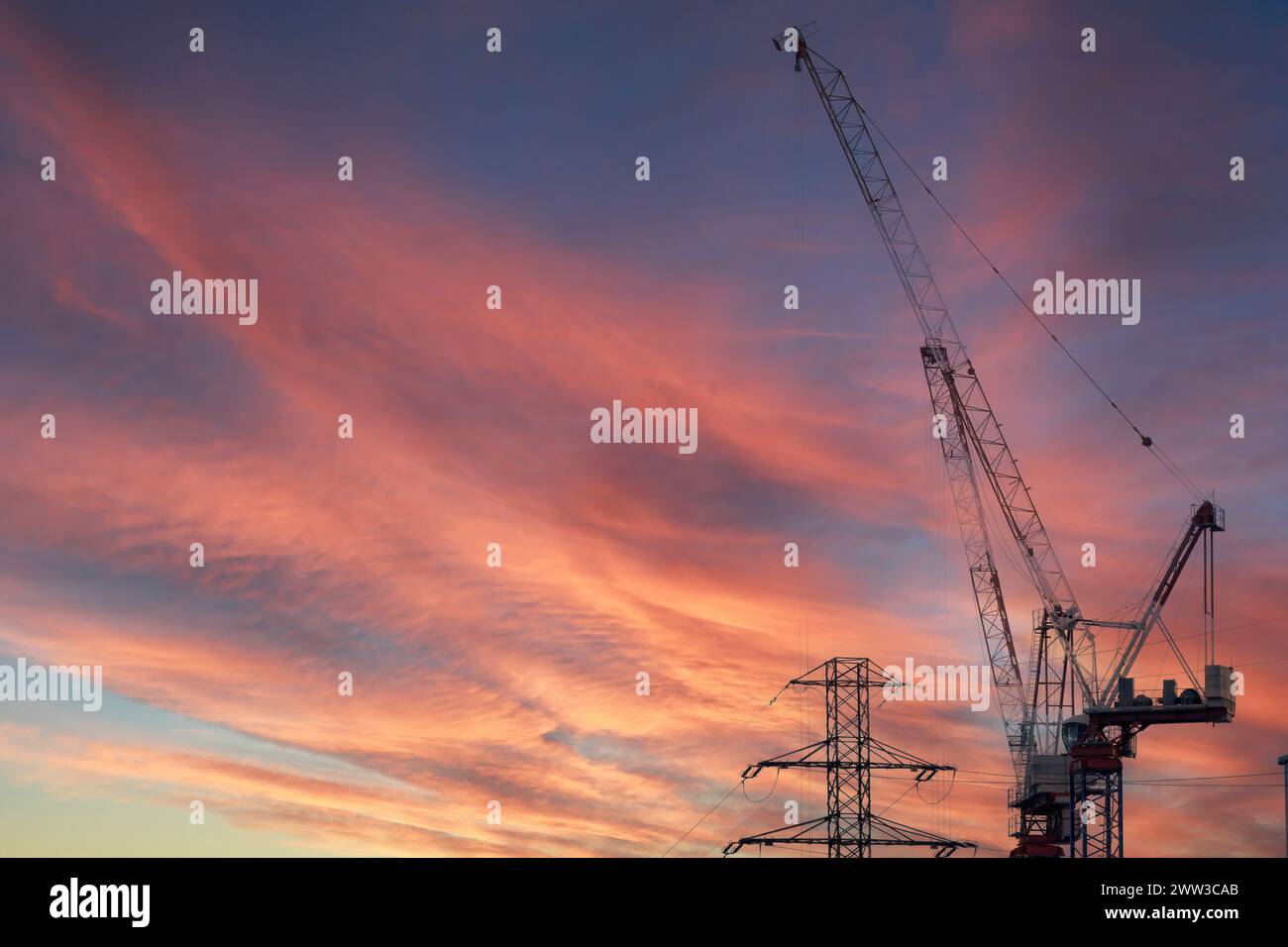 Una gru da costruzione e un pilone ad alta tensione sullo sfondo di un tramonto spettacolare, concetto di costruzione di nuove linee elettriche e infrastrutture. Foto Stock