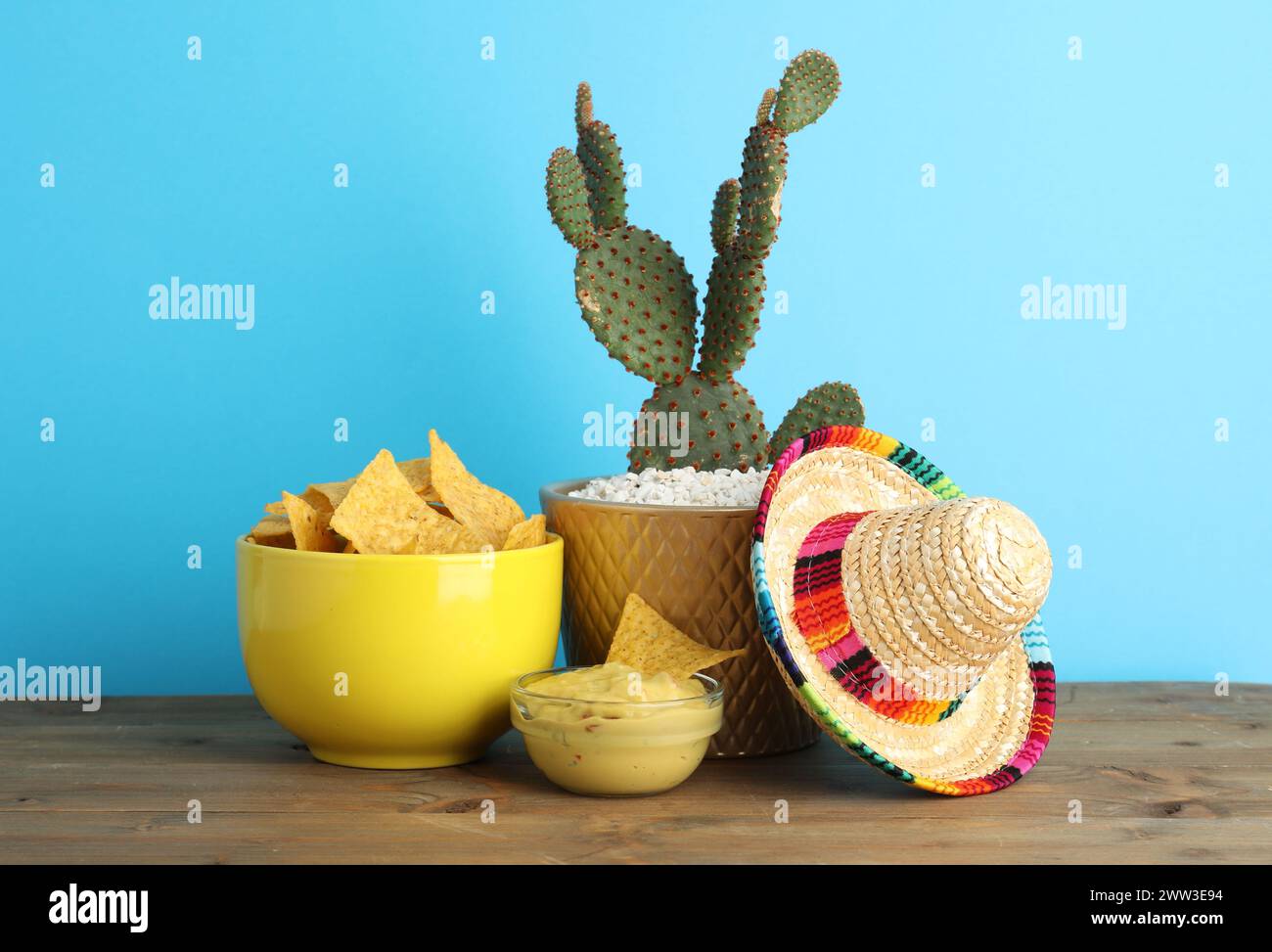 Cappello sombrero messicano, cactus, patatine di nachos e guacamole in ciotole su un tavolo di legno su sfondo azzurro Foto Stock
