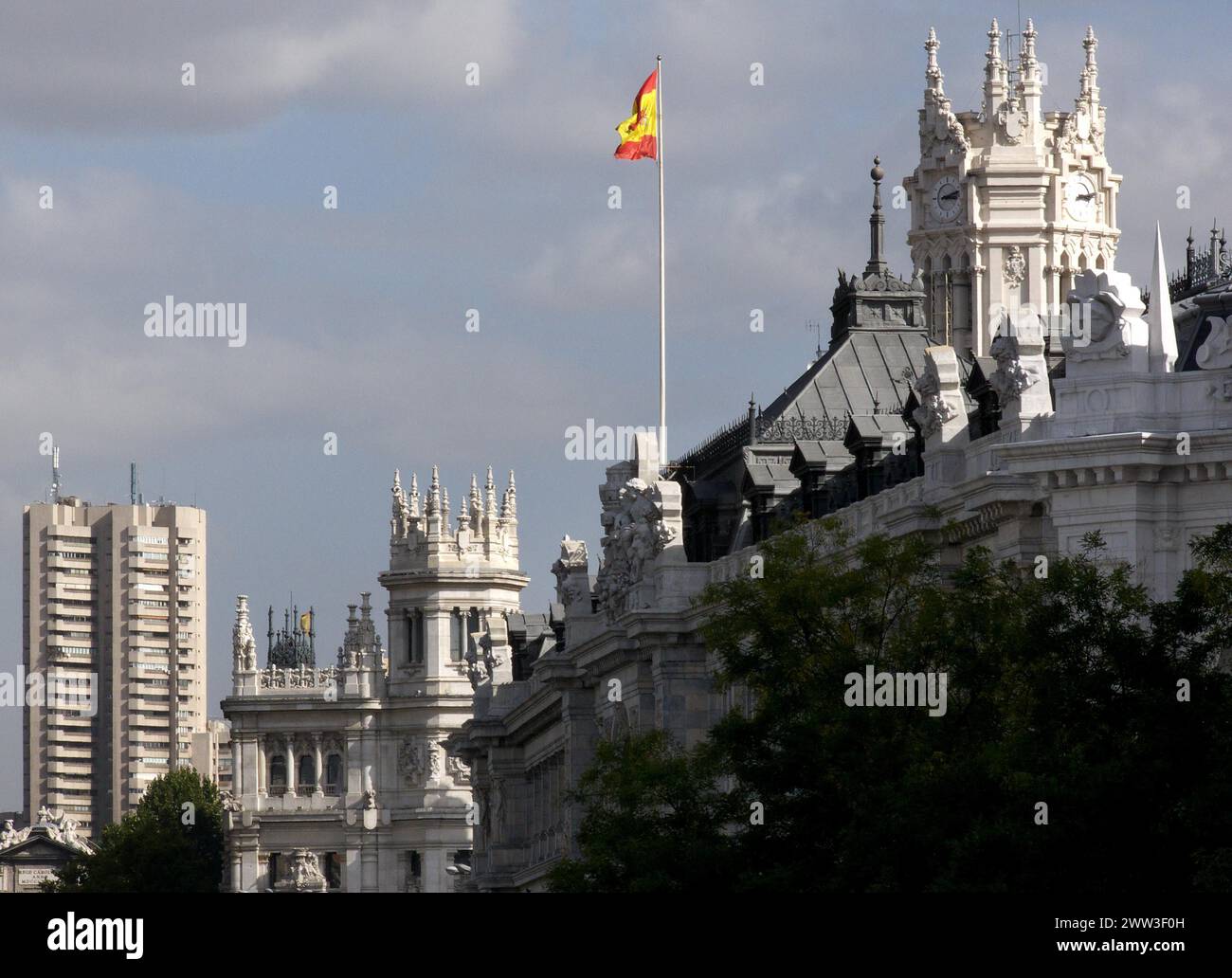 La bandiera spagnola vola sopra l'architettura opulenta sotto un cielo nuvoloso edificio delle poste di Madrid Spagna Foto Stock