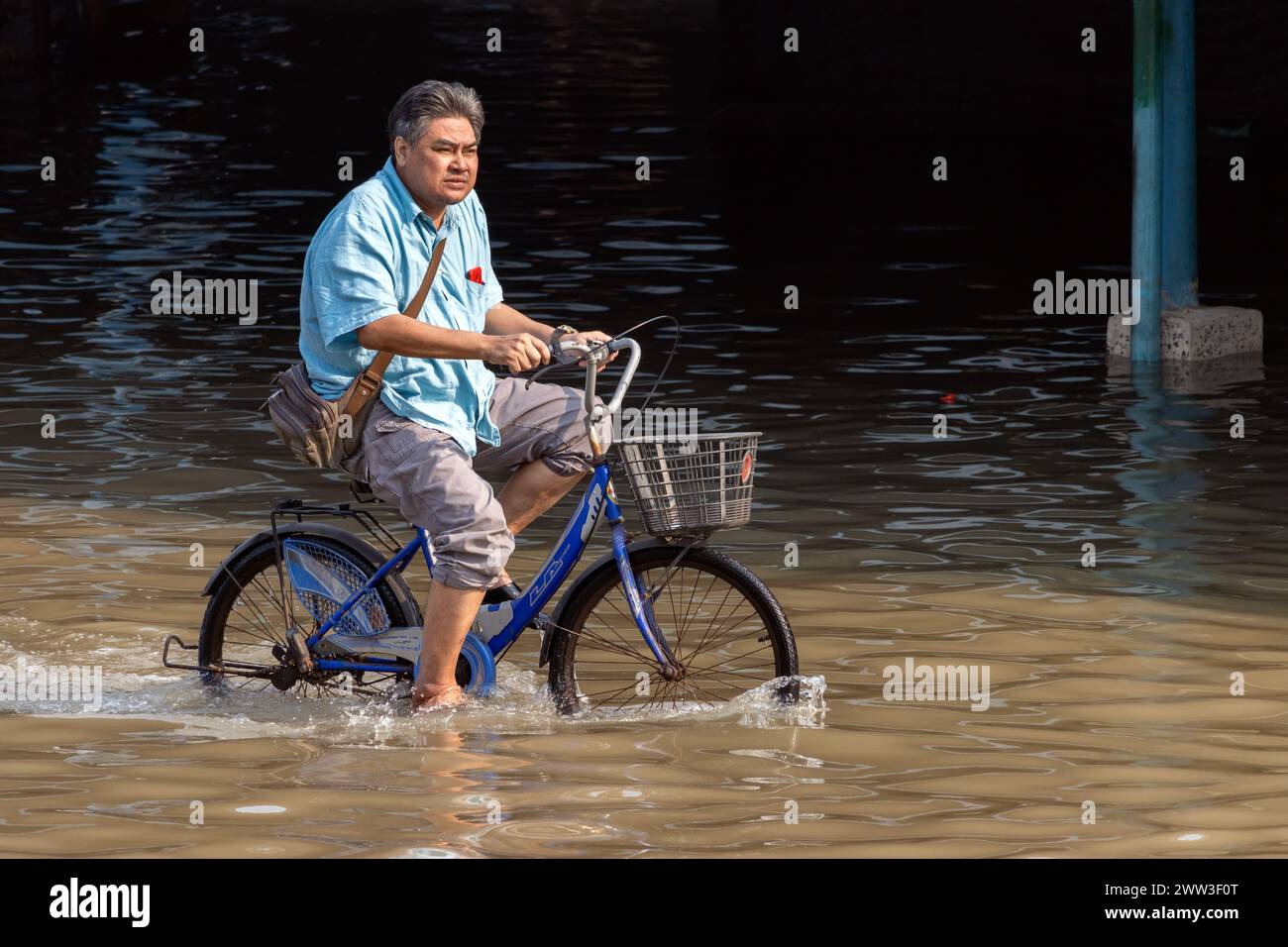 SAMUT PRAKAN, THAILANDIA, 11 febbraio 2024, Un ciclista guida una bicicletta su una strada allagata, Foto Stock