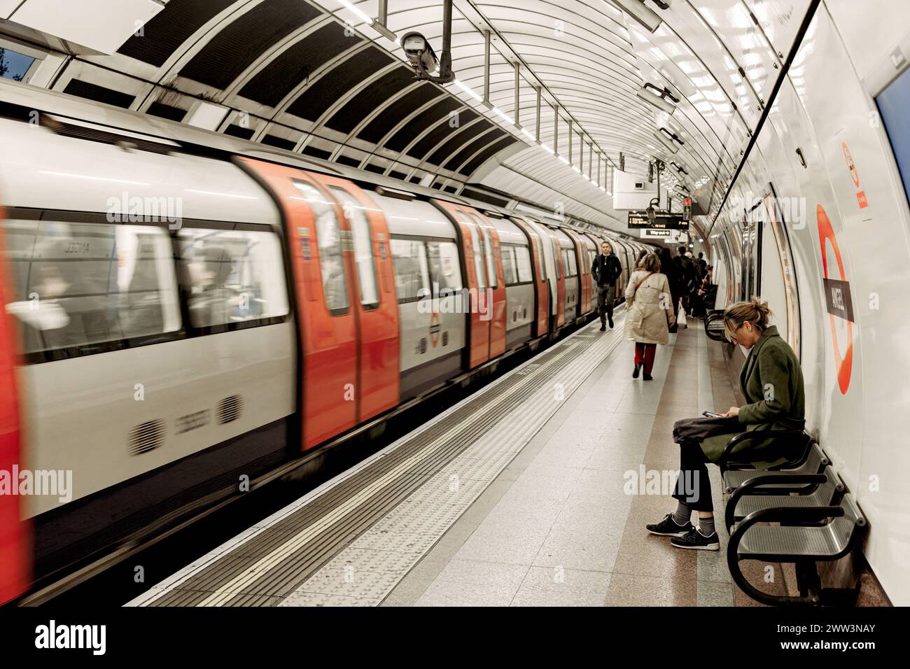 Alla stazione della metropolitana Angel di Londra, con persone che camminano o aspettano sul binario e un treno che parte dalla stazione. Foto Stock