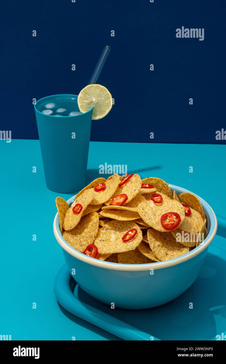 Rotondo di nachos di tortilla di mais con fette di peperoncino rosso in una ciotola con una bevanda fredda Foto Stock