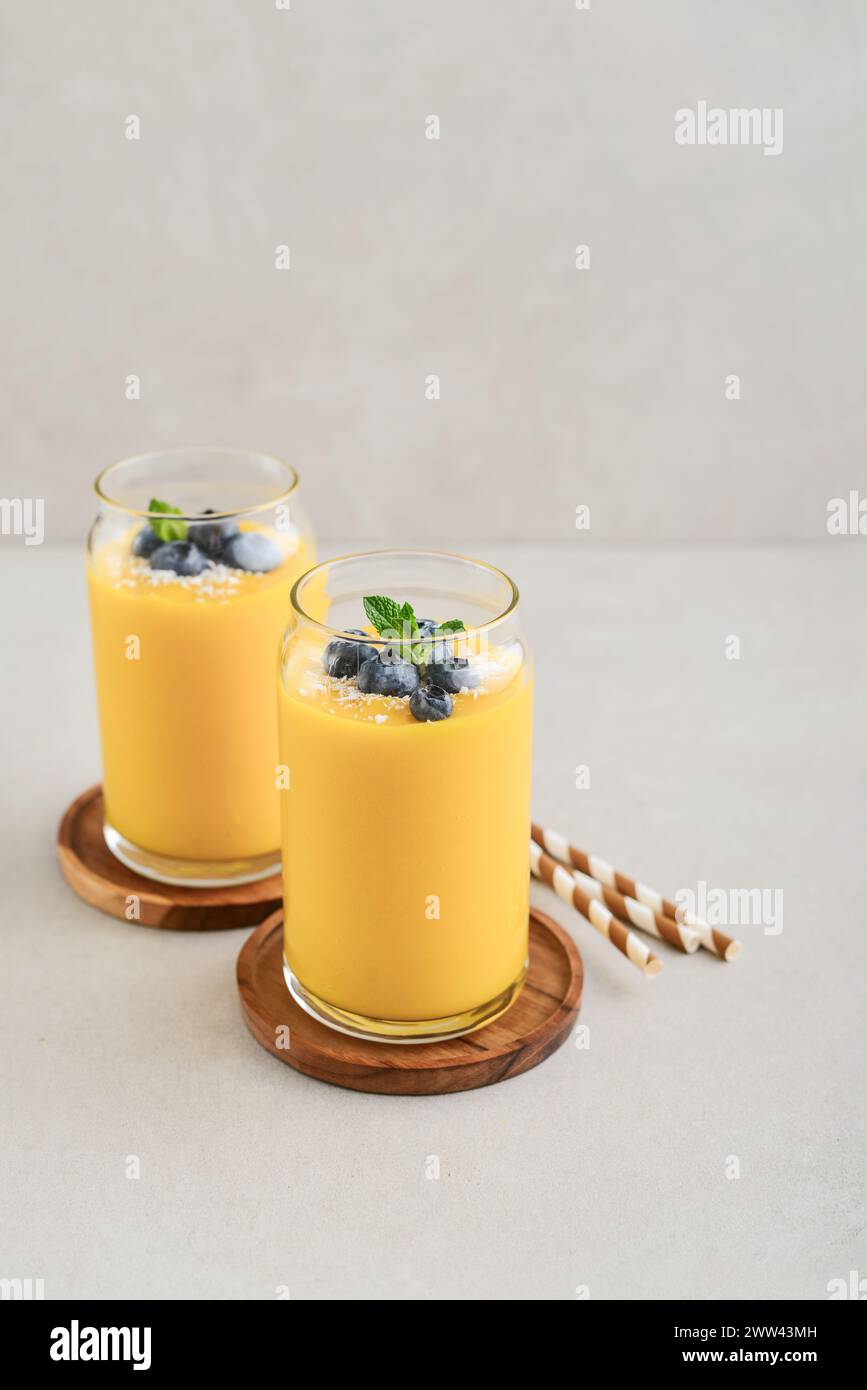 Frullato di mango rinfrescante e sano con scaglie di cocco e mirtilli freschi su sfondo chiaro Foto Stock