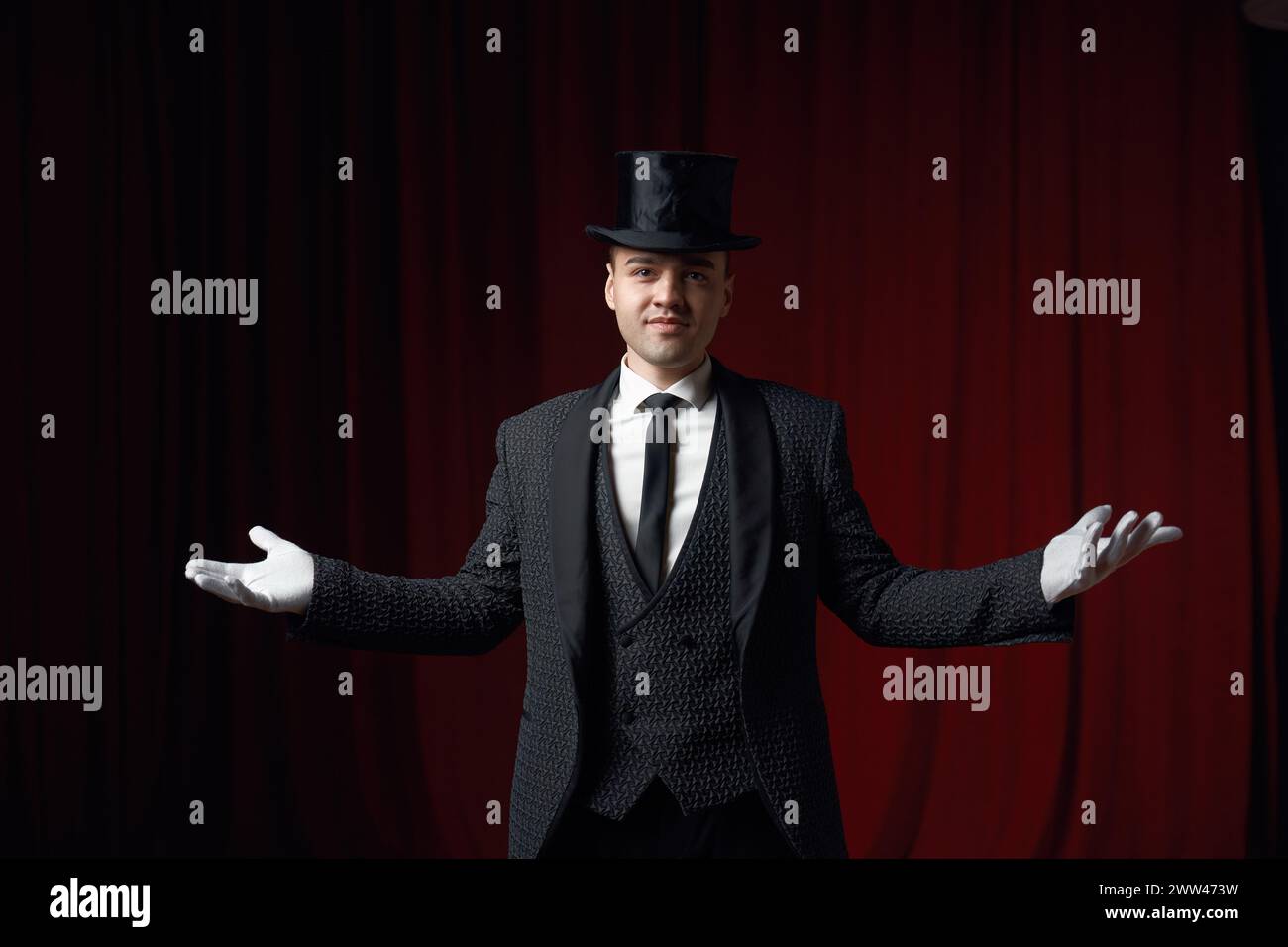 Sorridente showman alla moda o illusionista sul palco con un cappotto e un cappello a cappello Foto Stock