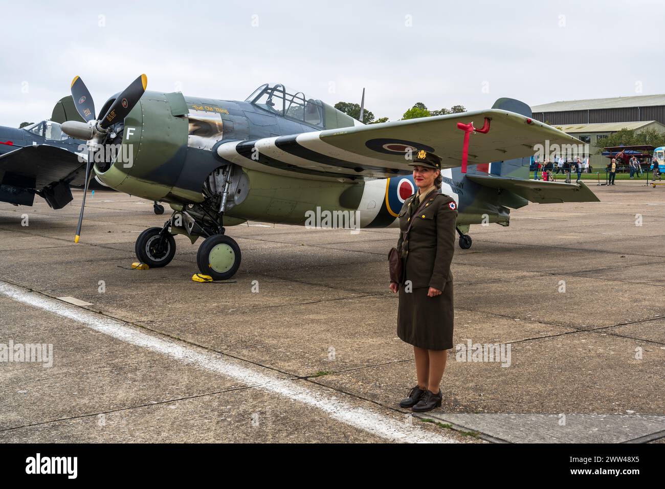 Donna in uniforme WAF si trova accanto a un Grumman FM2 Wildcat al Duxford Battle of Britain Air Show 2022, Duxford Airfield, Cambridgeshire, Inghilterra, Regno Unito Foto Stock