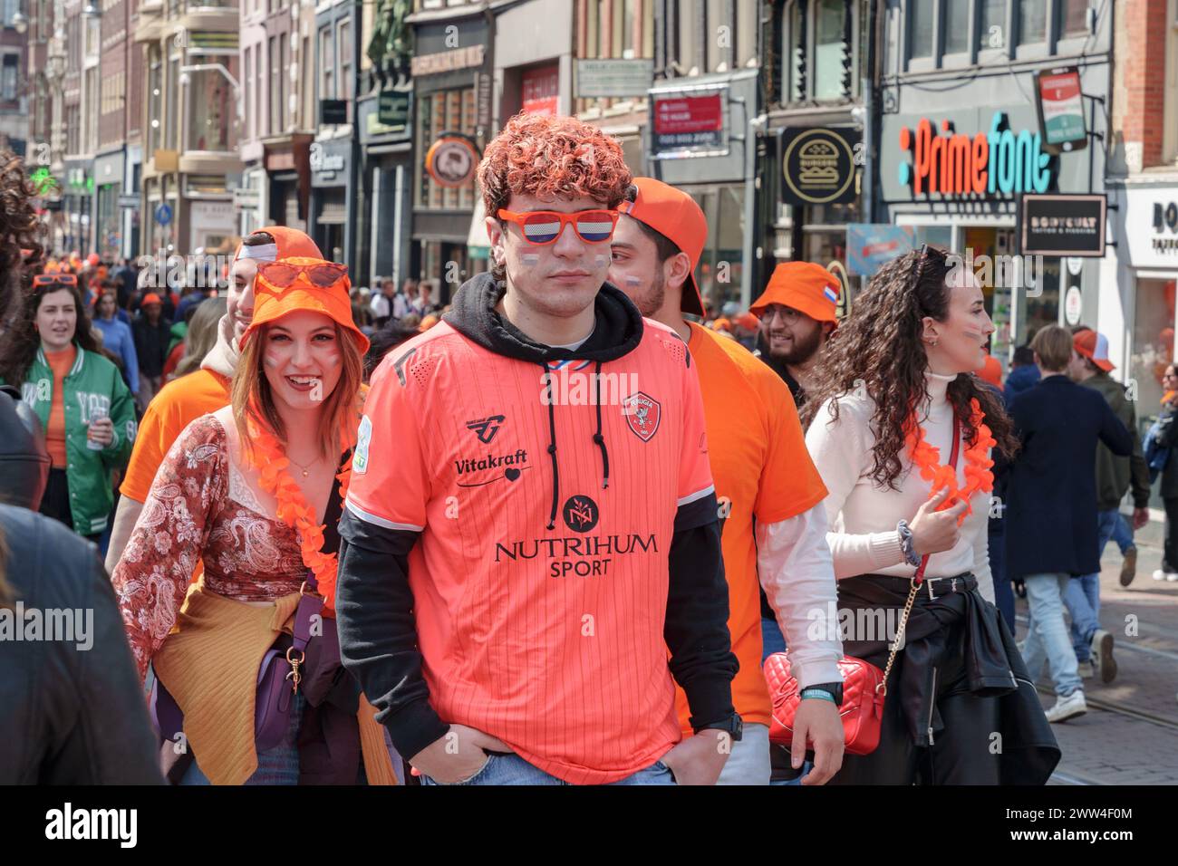 Una folla festeggia in una strada della città, indossando l'arancio. E' il giorno del Re, e sono nello spirito festivo tra i negozi - Paesi Bassi, Amsterdam, Foto Stock