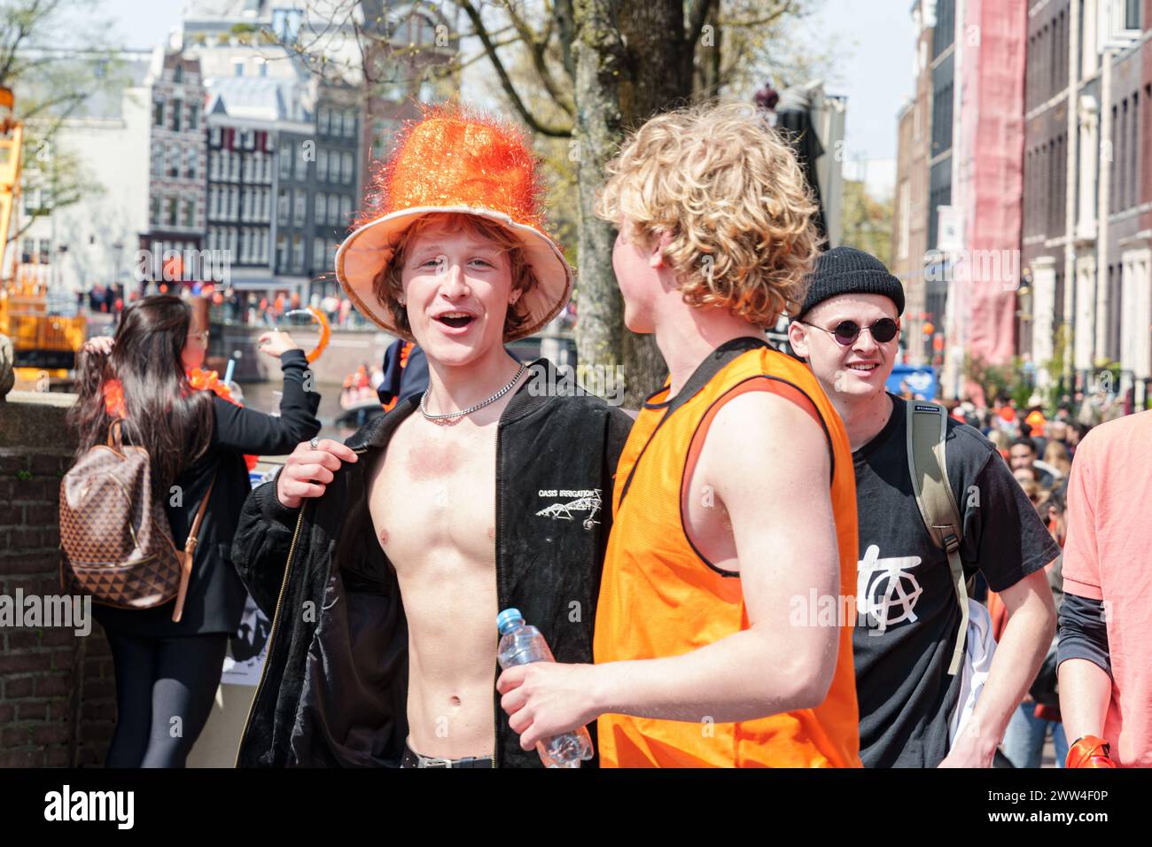 Una folla festeggia in una strada della città, indossando l'arancio. E' il giorno del Re, e sono nello spirito festivo tra i negozi - Paesi Bassi, Amsterdam, Foto Stock