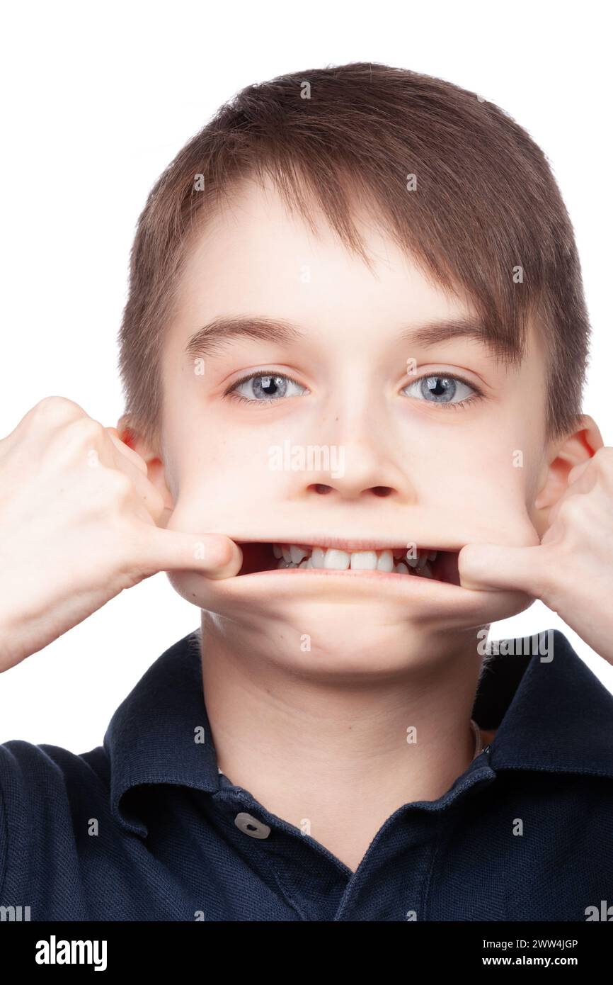 Un ragazzino che indossa una polo blu che si allunga la bocca con le dita, facendo un'espressione divertente. Ritratto in studio su sfondo bianco Foto Stock