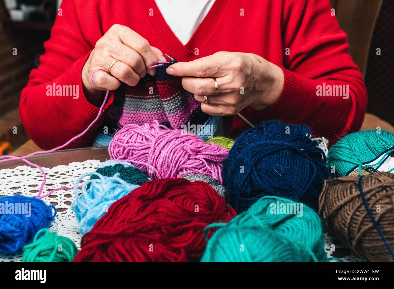 foto orizzontale di palle di lana e mani di donna anziana che cucisce un pezzo di abbigliamento con lana e aghi Foto Stock