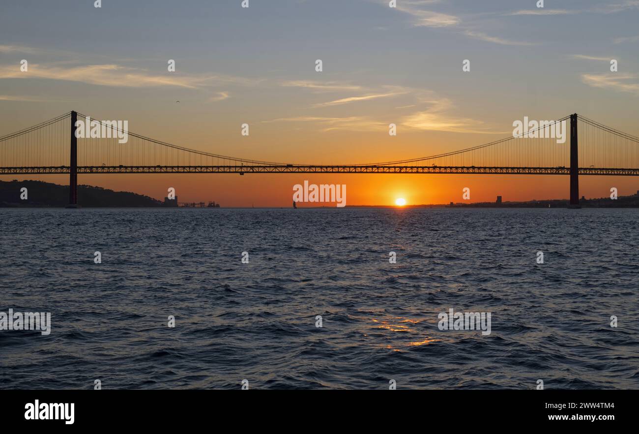 Lisbona, Portogallo, 14 marzo 2019: Una barca a vela naviga sotto il ponte 25 de Abril al tramonto. È un ponte sospeso che collega la città di Lisbo Foto Stock