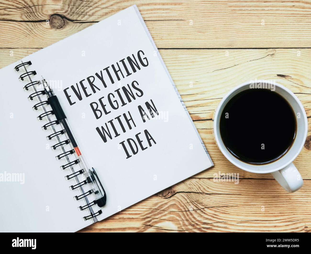Apri il quaderno con il testo "tutto inizia con un'idea" e una tazza di caffè su sfondo in legno. Foto Stock