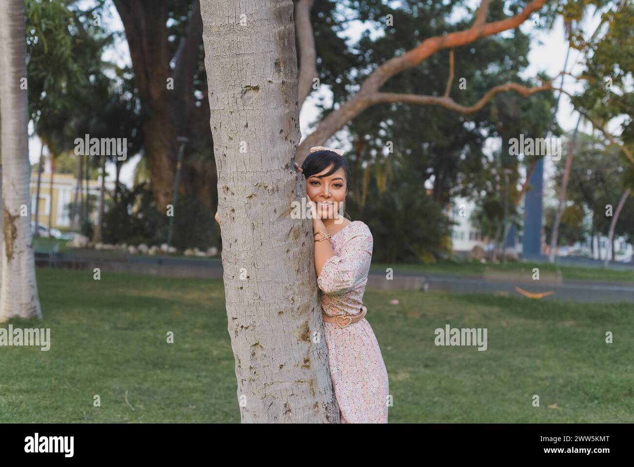 Donna che indossa un vestito e un fiocco che abbraccia un albero in un parco pubblico. Emozione positiva. Foto Stock