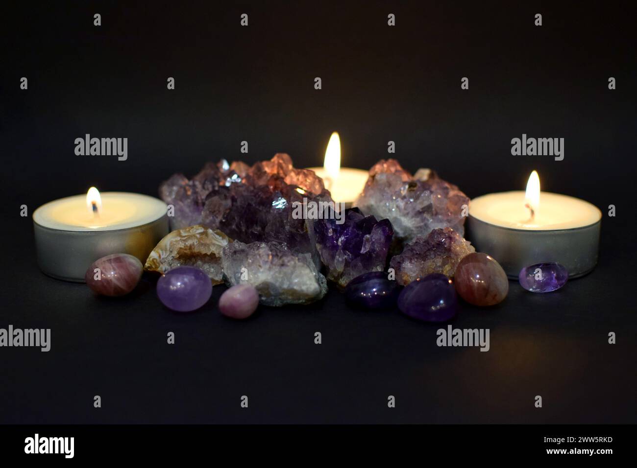 Bellissimo druzy viola con cristalli di ametista e candele accese al buio. Messa a fuoco selettiva. Foto Stock