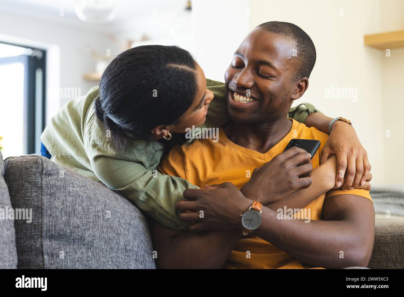Una coppia afroamericana condivide un momento di gioia sul divano di casa Foto Stock