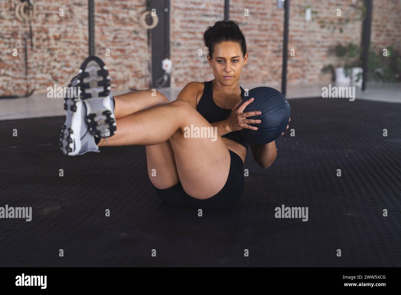 Una donna ispanica in forma sta eseguendo un esercizio addominale con una palla medica in una palestra Foto Stock