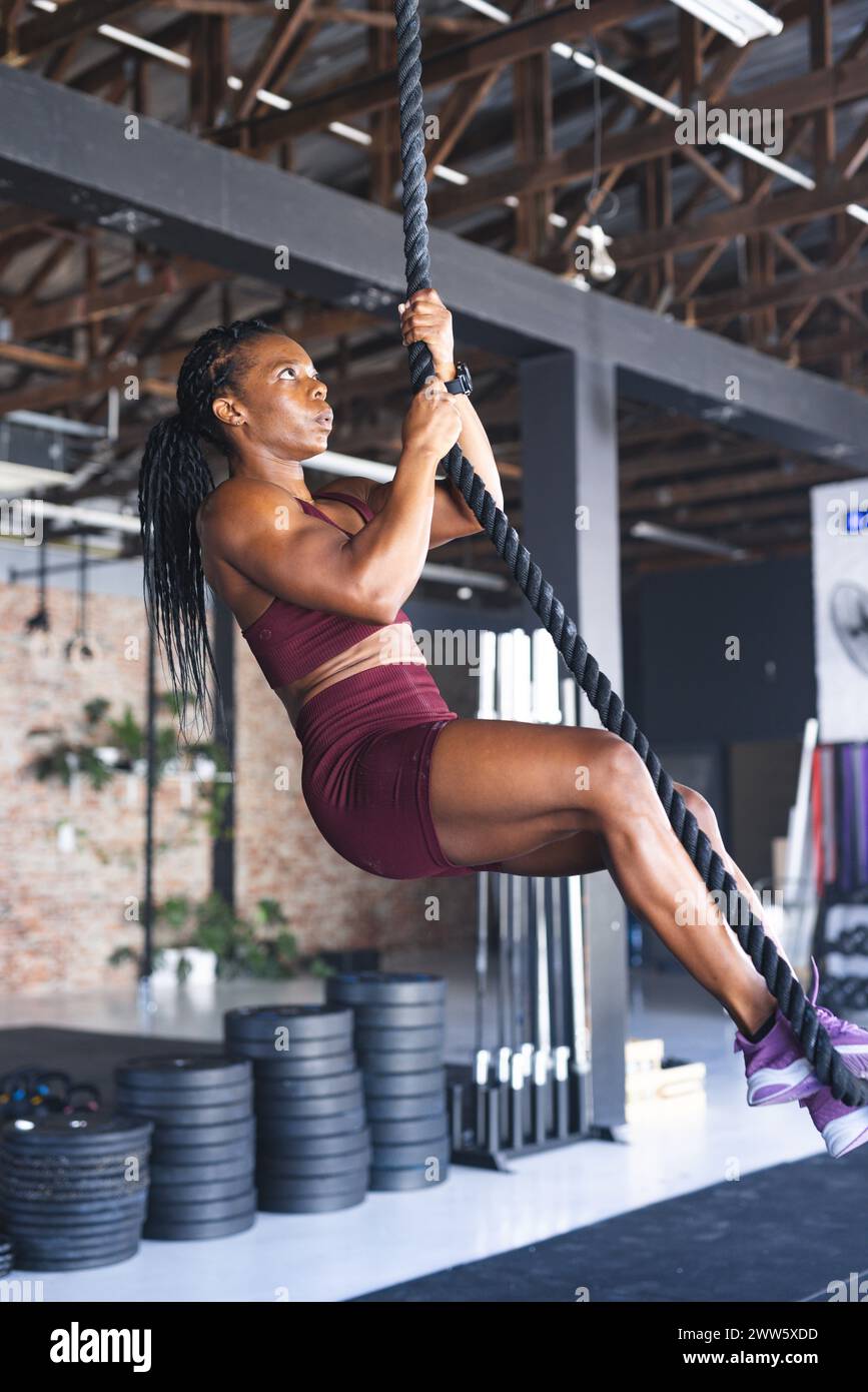 Una donna afroamericana forte si arrampica su una corda in palestra, mostrando forza Foto Stock