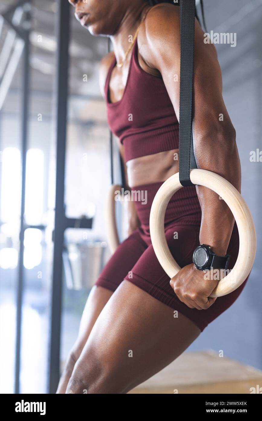 Una donna forte afroamericana in forma si sta allenando con anelli da ginnastica in palestra Foto Stock