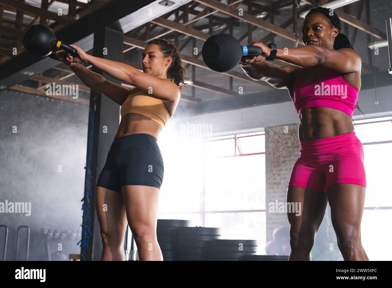 Due donne in forma si allenano con il kettlebell in palestra, una afroamericana Foto Stock